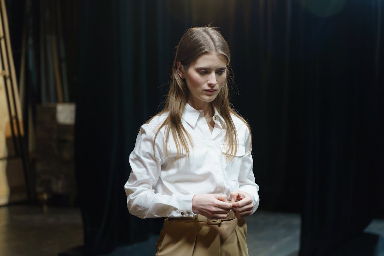 A young actress in a white shirt rehearsing alone on stage, captured thoughtfully.